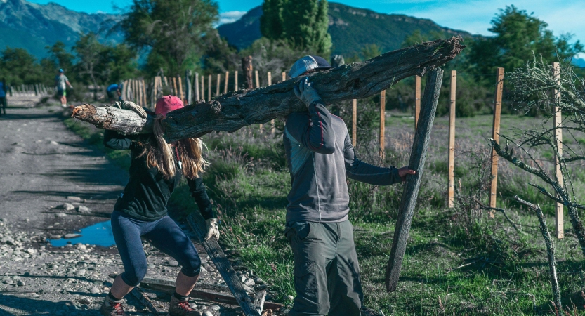 Two people carry a large piece of wood during a service project with outward bound. 